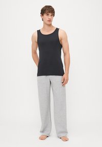 Schwarzes ärmelloses Tanktop kombiniert mit hellgrauen Sweatpants. Der Stoff ist glatt, und die Hose verfügt über zwei seitliche Taschen.