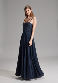 Abito da sera blu navy lungo fino al pavimento, con un corpino di perline, spalline sottili e una gonna in chiffon fluttuante. Presenta una parte superiore aderente con dettagli decorativi.