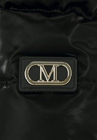 Svart pufferstoff med en blank overflate. Har en rektangulær svart lærpatch med en metallisk "CM"-logo i sølv.