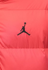 Logo de silueta negra de un jugador de baloncesto saltando con el balón sobre un fondo de tela acolchada roja.