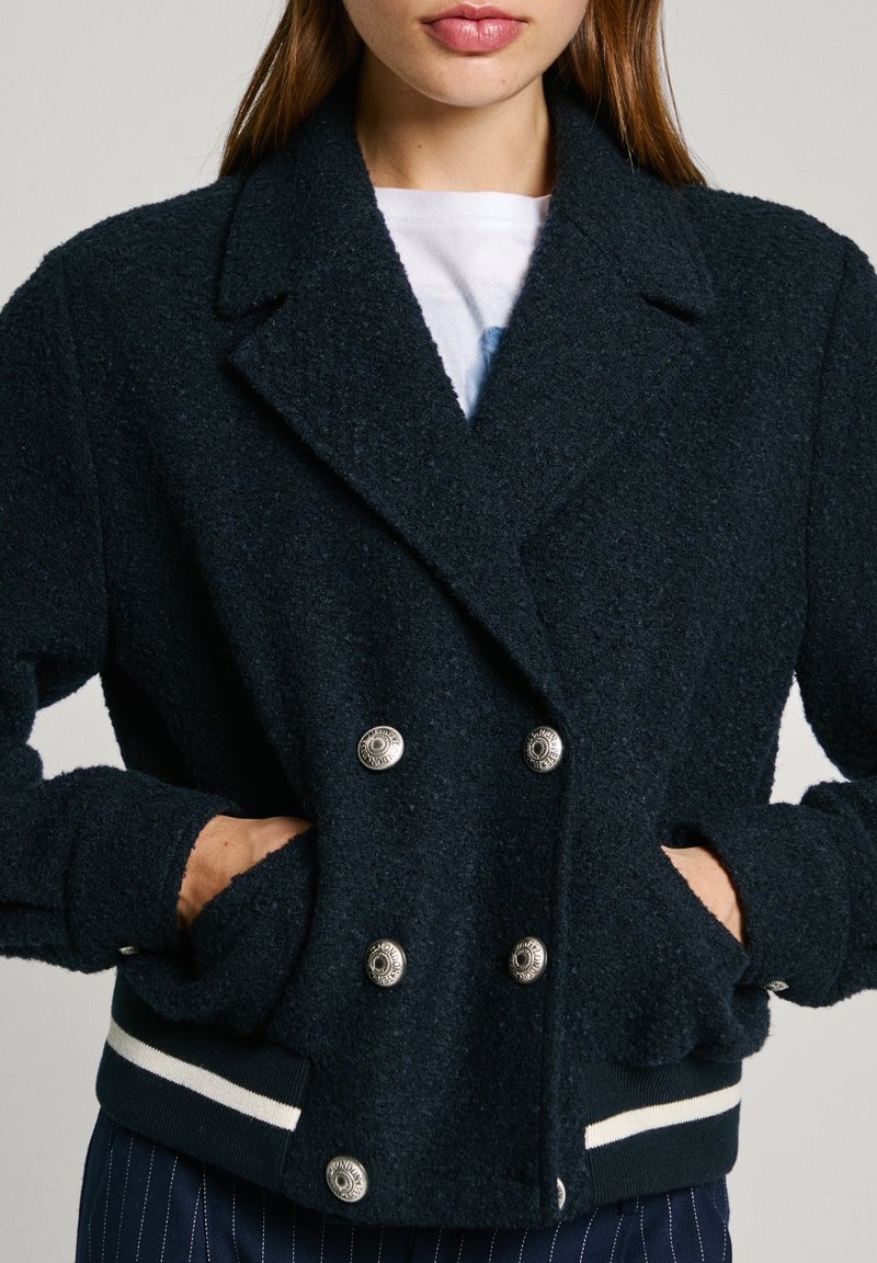 Marineblaue, strukturierte Doppelknopfjacke mit silbernen Knöpfen, seitlichen Taschen und gestreiftem Saum. Weiches Material mit lockerer Passform und weitem Kragen.