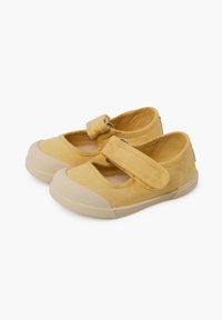 Scarpe di tela gialle con punta tonda, cinturino in velcro e suola in gomma beige. Presentano una texture liscia e dettagli di design minimi.