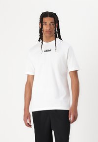 Balta medvilnės marškinėlė su trumpomis rankovėmis, su juodu "adidas" logotipu ant krūtinės. Nešiojami su juodomis kelnėmis, kurios turi laisvą siluetą.
