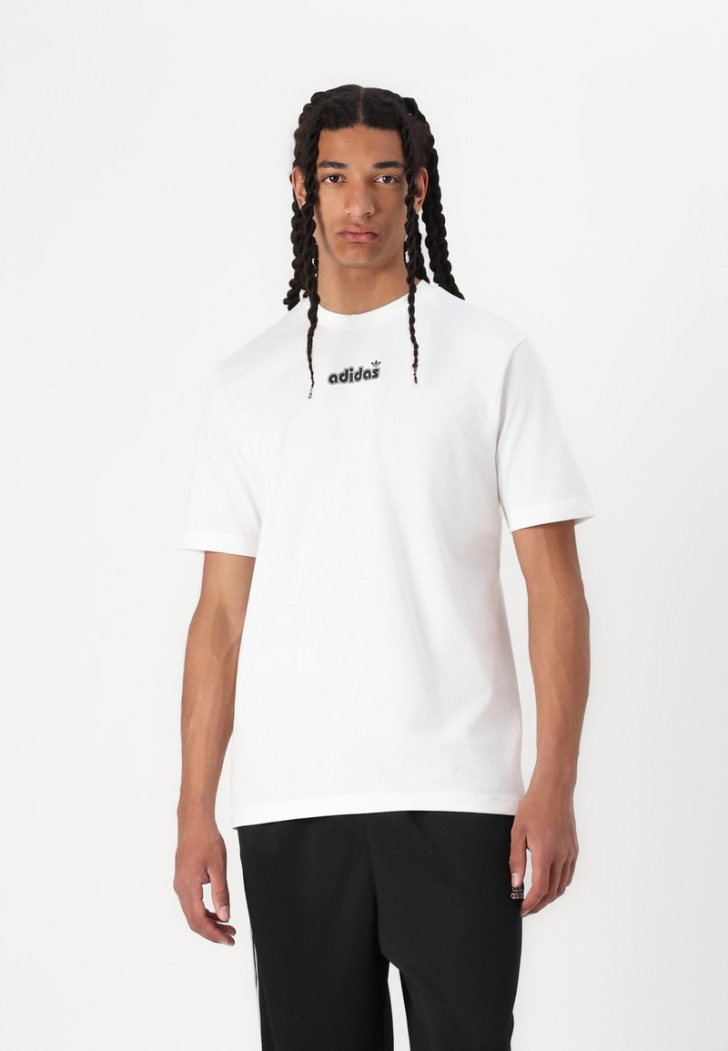 Balta medvilnės marškinėlė su trumpomis rankovėmis, su juodu "adidas" logotipu ant krūtinės. Nešiojami su juodomis kelnėmis, kurios turi laisvą siluetą.