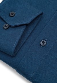 Zbliżenie na mankiet koszuli z niebieskiej teksturowanej tkaniny z dwoma czarnymi guzikami i szczegółowym przeszyciem.