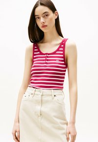 Rot-weiß gestreiftes, geripptes Tanktop mit Rundhalsausschnitt und drei Knöpfen an der Vorderseite, kombiniert mit einem cremefarbenen Jeansrock.