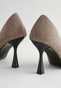 Cipele s visokom potpeticom i špicastim vrhom, izrađene od teksturirane metalne tkanine u nijansama bronze i srebra, sa elegantnom crnom stiletto potpeticom i suptilnim sjajem.