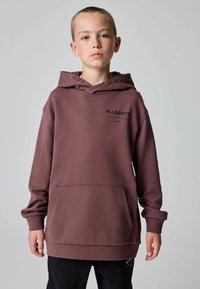 Hnedá mikina s kapucňou a klokania kapsou, so žebrovanými manžetami a detailom loga na hrudi. Hladký materiál a voľný strih.