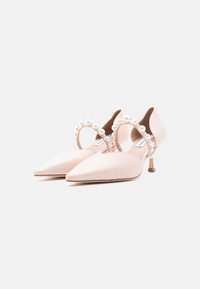 Ζευγάρι ανοιχτό ροζ μυτερές γόβες με μέτρια ψηλό τακούνι στιλέτο και λουράκια αστραγάλου στολισμένα με πέρλες σε λευκό φόντο.