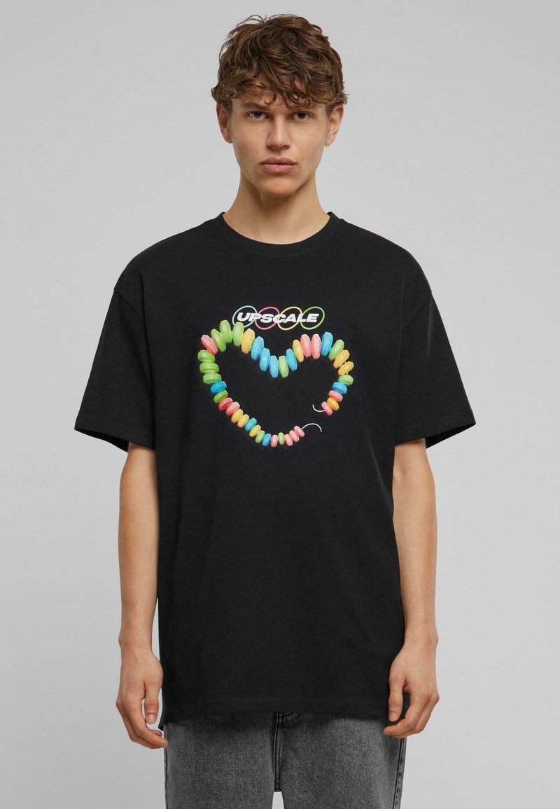 Camiseta negra de algodón con un gráfico de corazón colorido inspirado en dulces con "UPSCALE" arriba, de corte relajado y mangas cortas.