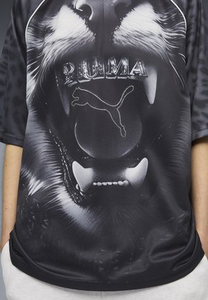 T-shirt de sport noir avec un graphisme détaillé de lion, le logo "PUMA" et une silhouette de puma étincelante faite de strass. Manches courtes.