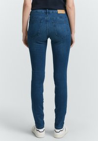 Jeans ajustados en denim azul medio, con una cintura alta, bolsillos traseros y un parche de cuero con el logo en la cinturilla. Textura suave.