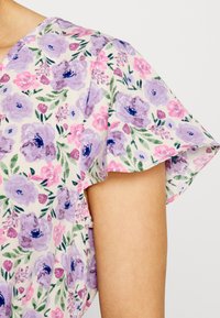 Tecido com padrão floral apresentando flores de lavanda e rosa com folhas verdes. Mangas curtas e alinhadas com frufrus e uma textura suave e leve.