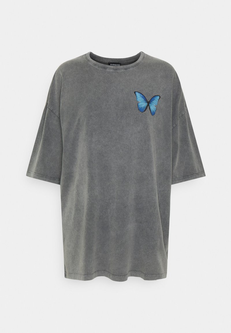 Camiseta gris de gran tamaño en material de algodón con mangas cortas. Presenta un estampado de mariposa azul en el lado izquierdo del pecho. Textura suave y desgastada.