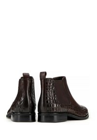 Botas Chelsea de cuero marrón con textura en relieve de cocodrilo, paneles laterales elásticos y tacones planos. El diseño es elegante con una punta redondeada.