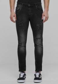 Fekete farmernadrág slim fit szabással, kopott részletekkel és megfakult felülettel. Öt zseb, cipzáras slicc és gombos zárás jellemzi.