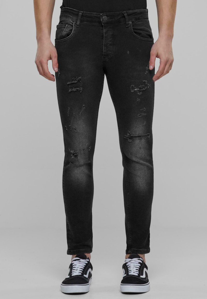 Fekete farmernadrág slim fit szabással, kopott részletekkel és megfakult felülettel. Öt zseb, cipzáras slicc és gombos zárás jellemzi.