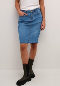 Modra denim suknja svinčnik z visokim pasom, sprednjimi žepi in ozkim krojem. V kombinaciji z črnimi in olivno zelenimi škornji do kolen.