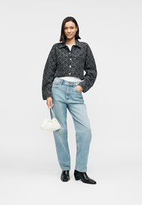 Μαύρο τζιν cropped μπουφάν με γεωμετρικό μοτίβο, σε συνδυασμό με ανοιχτόγαλανες ψηλόμεσες τζιν. Το μοντέλο κρατάει μια μικρή λευκή τσάντα χειρός. Μαύρα μποτάκια μέχρι τον αστράγαλο.