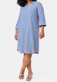 Robe à rayures bleues et blanches avec un col, des manches trois-quarts, et une coupe ample. Le tissu semble léger et lisse.