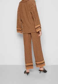 Brun mönstrad outfit som har en löst sittande topp och vida byxor, båda med kontrasterande ränder vid fållen. Svarta klackmules kompletterar looken.