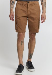 Brune cargo shorts laget av bomull, med sidelommer, rett passform og knappeåpning. Brukt med svarte joggesko.