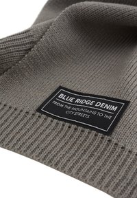 Siva pletena ruta z ribasto teksturo; vsebuje črno etiketo z napisom "BLUE RIDGE DENIM" v beli barvi in logotipom.
