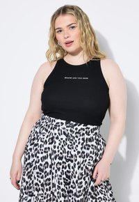 Top in cotone nero a costine con la scritta bianca "DOVE SEI ORA", abbinato a una gonna bianca plissettata con motivo leopardato nero e bottoni.