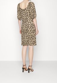 Eläinkuosilla varustettu mekko, jossa on pyöreä selkäosa, lyhyet puffihihat, polvenpituinen leikkaus ja pehmeä, kevyt kangas. Kengät mustat korot.