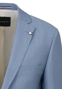Hellblaue Blazer aus strukturiertem Stoff, mit einer einzigen Brusttasche und einem silbernen Logo-Pin mit roten und blauen Akzenten am Revers.