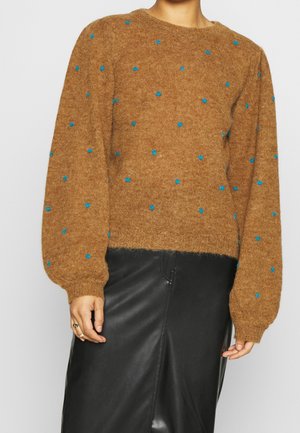 Pull marron duveteux à pois bleus avec manches ballon porté avec une jupe en cuir noire sur une personne debout.