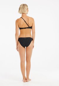 Čierny bikiny set s topom na jedno rameno, ktorý má textúrované pruhy. Spodný diel je nízko vyrobený, farba a vzor sú zhodné.