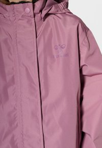 Różowa kurtka wykonana z gładkiego, lekkiego materiału. Posiada zamek błyskawiczny i zapięcie na guziki, regulowany kaptur oraz tłoczone logo na piersi.