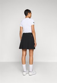 Gonna nera a pieghe con vita media, abbinata a una maglietta attillata bianca a maniche corte. Calze bianche e scarpe sportive completano il look.