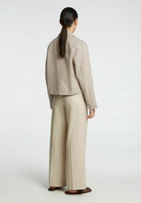 Chaqueta de punto beige con cuello alto, corte relajado y costuras visibles; combinada con pantalones beige de corte holgado y zapatos oscuros tipo slip-on.
