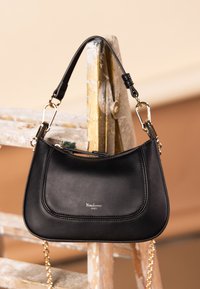 Svart läderhandväska med en böjd form, guldfärgade metallaccent och kort handtag. Har en silverfärgad logga präglad på framsidan.