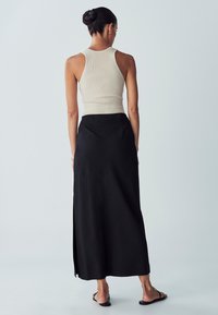 Světle béžový žebrovaný tílko spárované s černou, volně splývavou maxi sukni s bočním rozparkem, která ukazuje hladkou látku a minimalistický design.