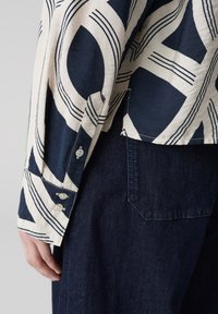 Camicia bianca e blu marina a fantasia con maniche lunghe, polsini abbottonati, texture morbida e orlo spaccato, abbinata a pantaloni in denim blu scuro.