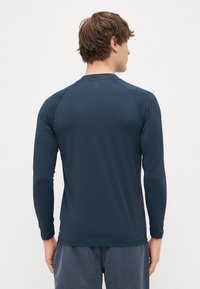 Μακρυμάνικο πουκάμισο ναυτικού χρώματος από λείο ύφασμα. Διαθέτει στρογγυλή λαιμόκοψη και ράγκελαν μανίκια. Επίπεδες ραφές με ελάχιστη λεπτομέρεια branding στο στρίφωμα.