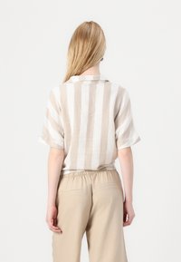 Camicia di lino a strisce verticali beige e bianche, con colletto, maniche corte e vestibilità morbida. Abbinata a pantaloni beige chiaro.