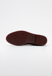 Suela de zapato de goma roja con una superficie texturada que presenta indentaciones circulares, un logo rectangular y un tacón plano.