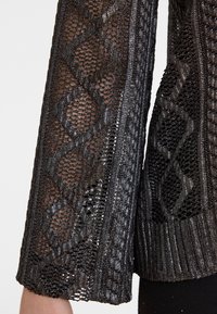 Zwarte gebreide trui met een gestructureerde open weving en geometrische patronen, geribde manchetten en glanzende accenten.