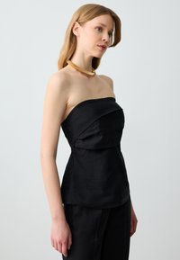 Zwart strapless top gemaakt van lichtgewicht stof, met een gedrapeerd ontwerp en een aansluitende taille. Versterkt met een gladde afwerking.