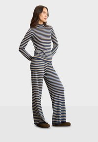 Pajama set s prugastim uzorkom koji se sastoji od uskog turtleneck-a i širokih hlača u plavoj, zlatnoj i krem boji. Mekana tekstura s opuštenim krojem.