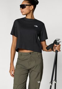 Μαύρο κοντομάνικο t-shirt με το λογότυπο The North Face, συνδυασμένο με χακί παντελόνι με τσέπες και ένα πεζοπορικό μπαστούνι με γκρι λαβή.