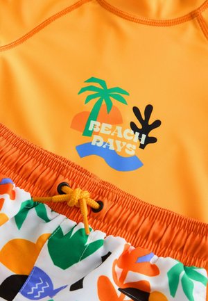 Maglietta da nuoto arancione con design grafico che presenta palme e la scritta "BEACH DAYS", abbinata a pantaloni da bagno con motivi. Coulisse gialla in vita.