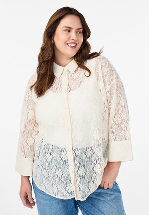 Spitzenbluse in Off-White mit Knopfleiste, kragenlosem Halsauschnitt und drei Viertelärmeln. Ausgeprägtes florales Muster über die gesamte Fläche.