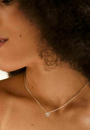 Collana in argento con una catena delicata, caratterizzata da un pendente a forma di cuore con texture. La collana si posiziona appena sopra la clavicola.