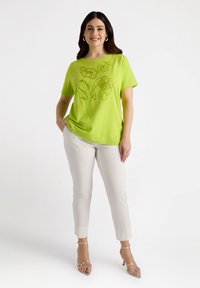 Top corto de manga corta en verde lima con bordado floral; combinado con pantalones ajustados de color beige claro y sandalias de tacón alto plateadas con tiras.