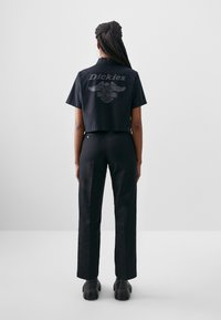 Cropped black t-shirt featuring “Dickies” logo and Harley-Davidson graphics on the back. Worn with fitted black pants and black footwear.